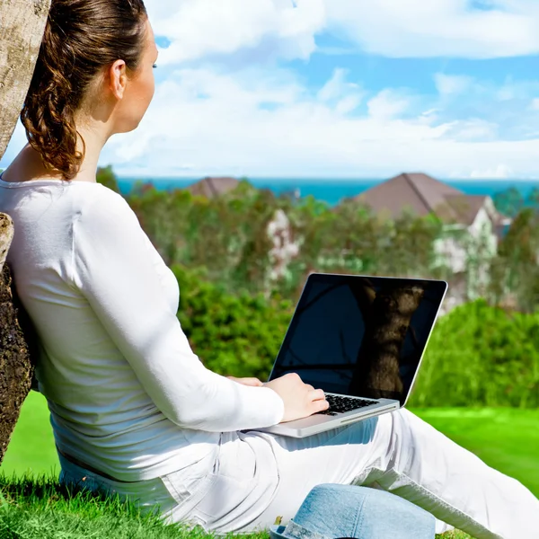 Jovem mulher sentada debaixo da árvore com laptop e sonhando. Idílicos — Fotografia de Stock