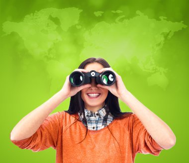 Young woman looking through binoculars against world map at back clipart