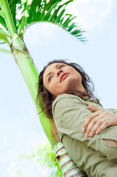 Retrato de una joven mujer bonita apoyada en la palmera y disfrutando —  Fotos de Stock