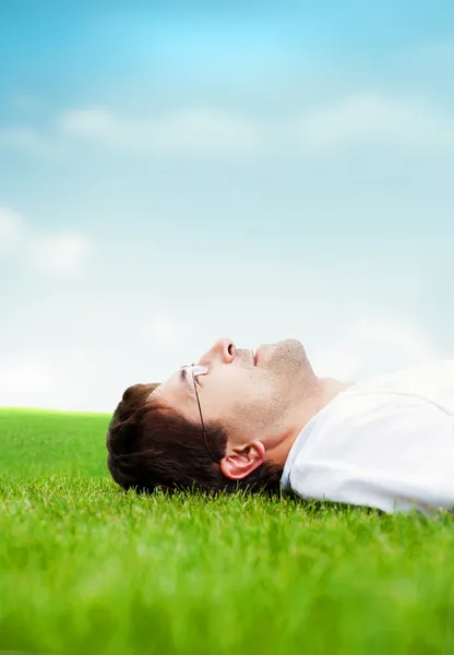 Mladý dobře vyhlížející muž v bílé košili leží na trávě a při pohledu na oblohu — Stock fotografie