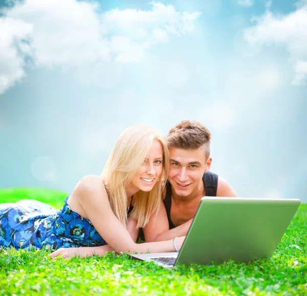 Portrait of young couple outdoor resting on green grass and usin — Stock Photo, Image
