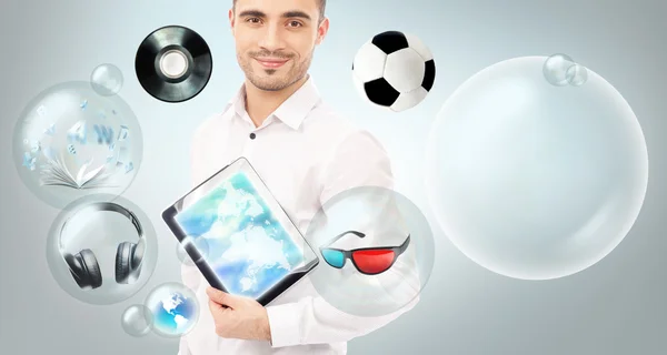 Homme beau adulte tenant un ordinateur tablette. Icônes de différents objets volent autour . — Photo