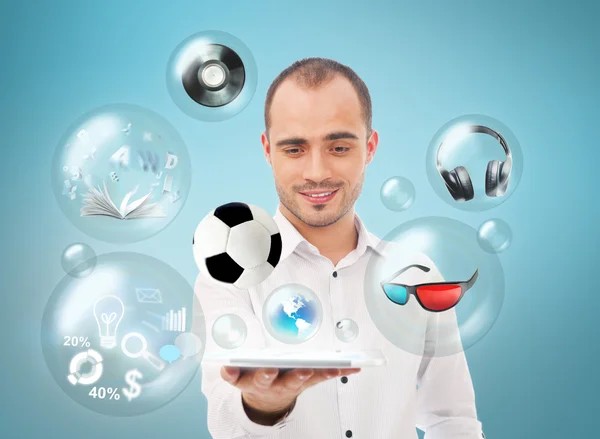 Hombre guapo adulto sosteniendo la tableta. Iconos de diferentes objetos están volando alrededor . — Foto de Stock