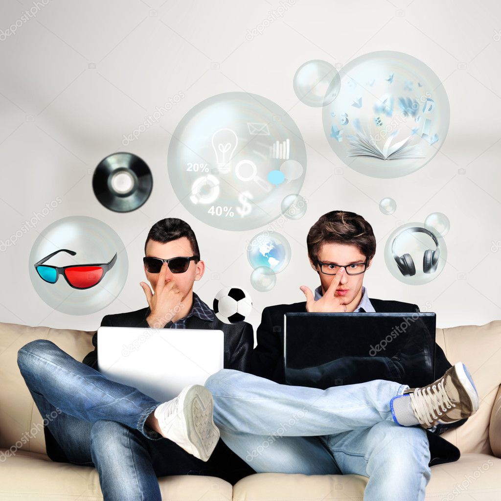 Two young gamers sitting together on sofa and using their laptop