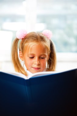 Image of smart child reading interesting book in classroom clipart