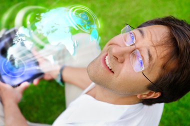 Adult man sitting on grass in park and using his tablet computer clipart