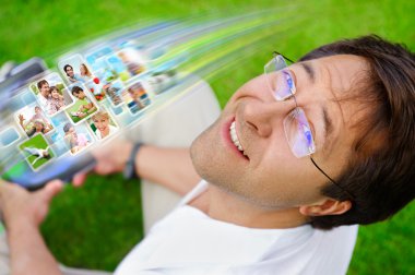 Adult man sitting on grass in park and using social media to loo clipart