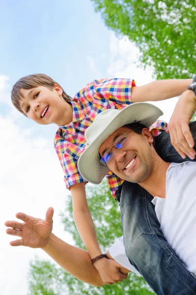 Porträtt av leende far att ge sin son piggyback rida utomhus — Stockfoto