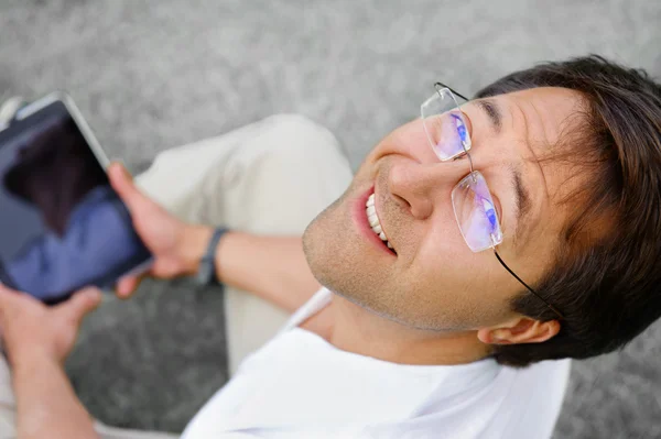 Bonito homem relaxado e positivo está surfando em seu tablet — Fotografia de Stock