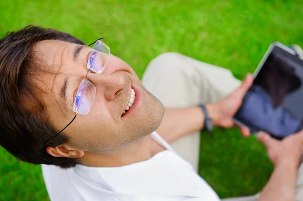 Дорослий чоловік сидить на траві і використовує свій планшетний комп'ютер — стокове фото