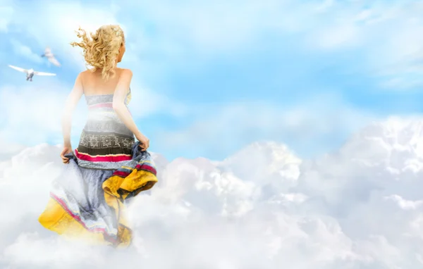 Young woman running across the clouds in the sky — Stock Photo, Image
