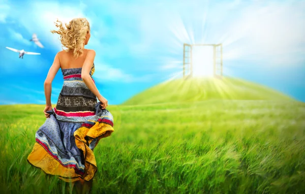 Mujer joven corriendo a través de hermoso campo a la puerta luminosa brillante en una colina — Foto de Stock
