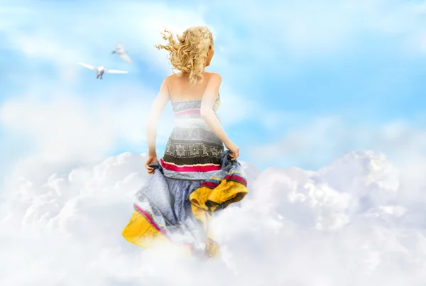 Young woman running across the clouds in the sky — Stock Photo, Image