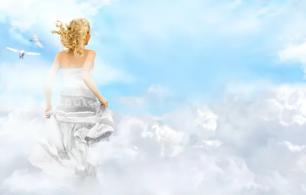 Jovem mulher correndo através das nuvens no céu — Fotografia de Stock