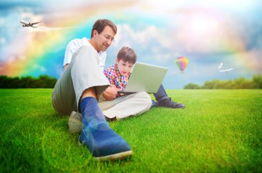 Adult man and his little son sitting on a grass at park and havi clipart