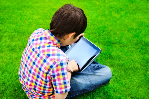 Menino sentado na grama e usando o computador tablet — Fotografia de Stock