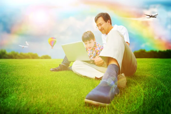 Hombre adulto y su pequeño hijo sentado en una hierba en el parque y havi —  Fotos de Stock