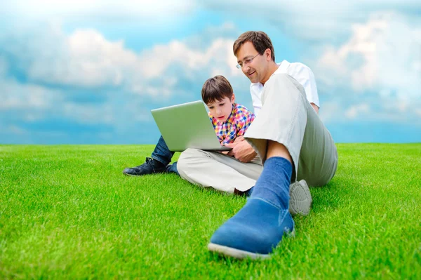 Отец и сын в парке улыбаются и веселятся с ноутбуком — стоковое фото
