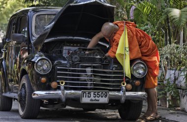 Thailand, Chiang Mai, a Buddhist monk is trying to fix his old car's engine clipart