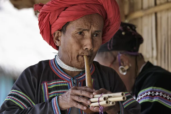 Thailand, chiang mai, karen long neck hill tribe village (kayan lahwi), karen man in traditionellen trachten, die eine flöte spielen — Stockfoto