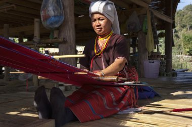 Thailand, Chiang Mai, Karen Long Neck hill tribe village (Kayan Lahwi), a Karen woman in traditional costumes is making a carpet clipart
