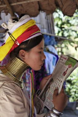 Tayland, chiang mai, karen uzun boyunlu tepe kabile Köyü (baan tong lhoung), uzun boyunlu kadın geleneksel kostümleri bir dergi okuma. 5 veya 6 yıl olduğunda kadınlar pirinç halkalar kendi boynuna koy.