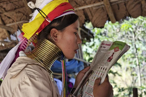 Thailand, Chiang Mai, Karen Long Neck hill tribe village (Baan Tong Lhoung), Long Neck woman in traditional costumes reading a magazine. Women put brass rings on their neck when they are 5 or 6 years — Stock Photo, Image