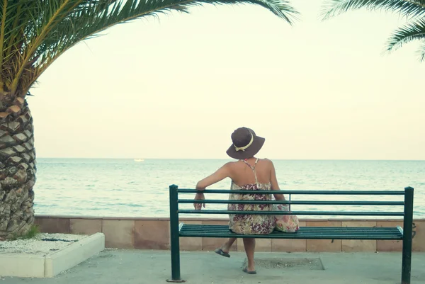 Молодая женщина сидит на скамейке у моря — стоковое фото