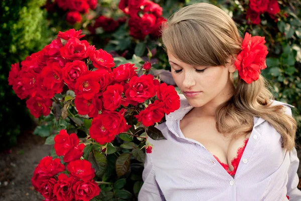 Young woman in flower garden smelling red roses — Stock Photo, Image