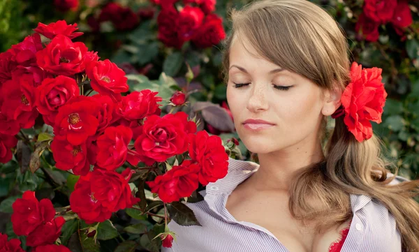 Young woman in flower garden smelling red roses — Stock Photo, Image