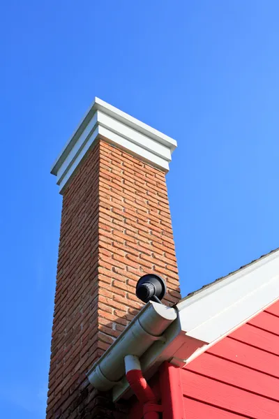 Orange brick pipe and black roof on blue sky — Stock Photo, Image