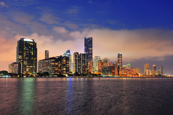 Miami city skyline panorama at dusk with urban skyscrapers over sea with reflection
