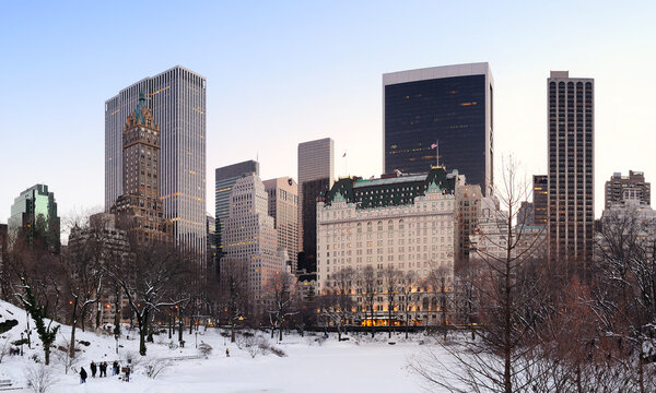 New York City Manhattan Central Park panorama in winter with snow, freezing lake and skyscrapers at dusk.