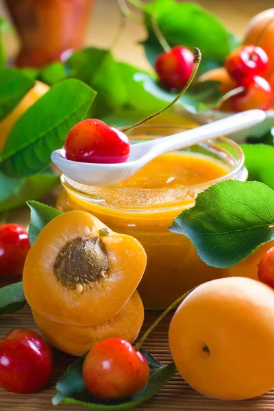 Marmellata di albicocche e ciliegie in vaso e frutta fresca con foglie — Foto Stock