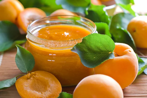 Apricot jam in jar and fresh fruits with leaves — Stock Photo, Image