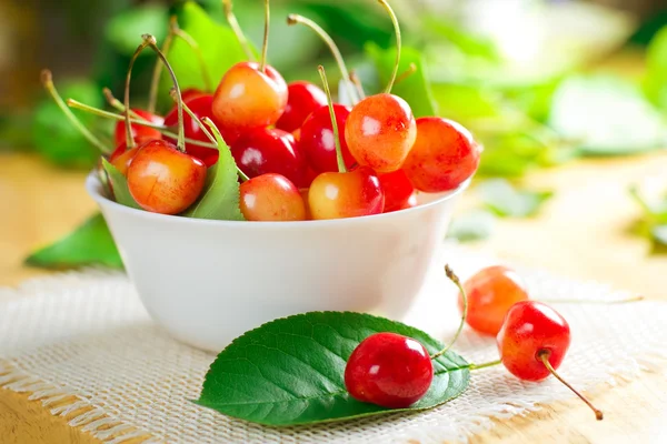Wet sweet cherry on the white bowl and fresh green leaves — Stock Photo, Image