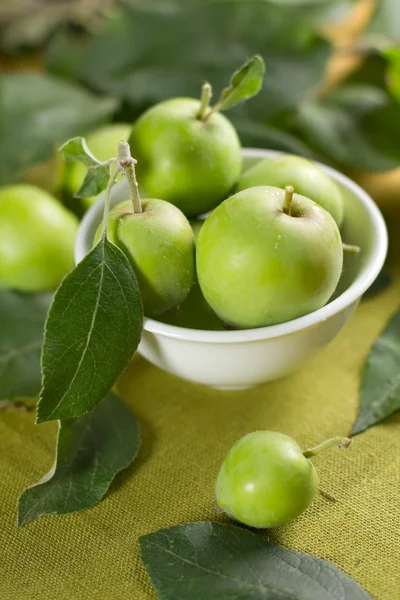 Kleine Äpfel in der Schüssel und grüne Blätter — Stockfoto
