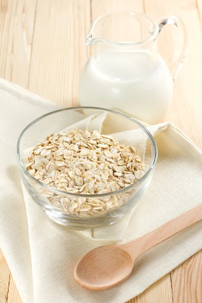 Oat flaks on a glass boel and jug of milk — Stock Photo, Image