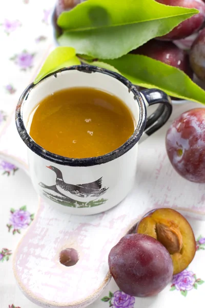 Plum juice and fresh fruits with leaves — Stock Photo, Image