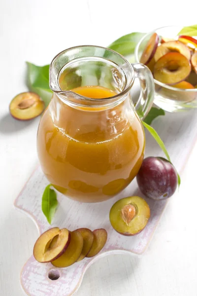 Сливовый сок и свежие фрукты с листьями — стоковое фото