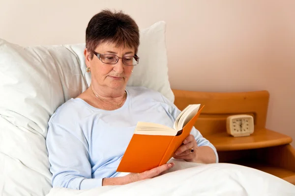 Senior en el hogar de ancianos en la cama leyendo el libro — Foto de Stock