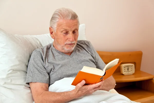 Starszy w domu opieki, czytać książki w łóżku — Zdjęcie stockowe