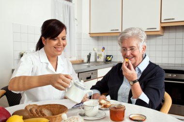 Nurse helps elderly woman at breakfast clipart