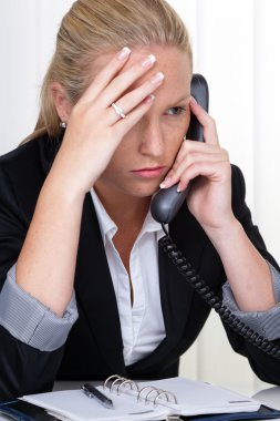 Frustrated woman holding a telephone in the office clipart