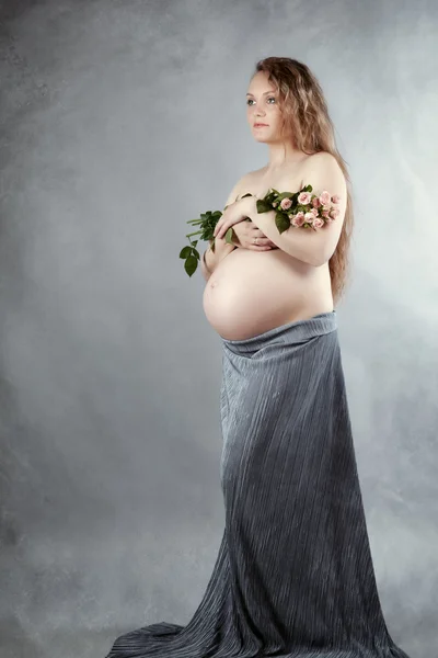 Vackra gravid kvinna med blommor i hennes armar, studio — Stockfoto