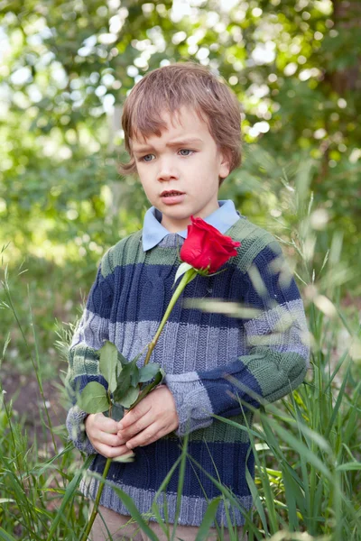 Smutný chlapeček hospodářství rudá růže v ní ruku, park — Stock fotografie