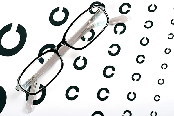 Óculos pretos em um gráfico de teste de visão — Fotografia de Stock