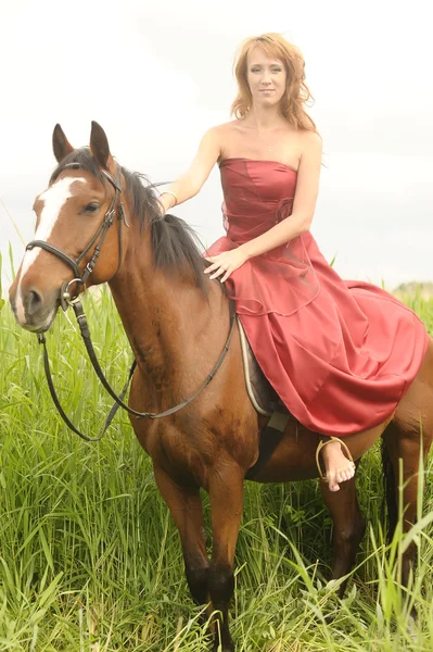 Žena v červených šatech na koni — Stock fotografie