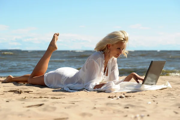 Mulher loira feliz em uma praia com um laptop — Fotografia de Stock