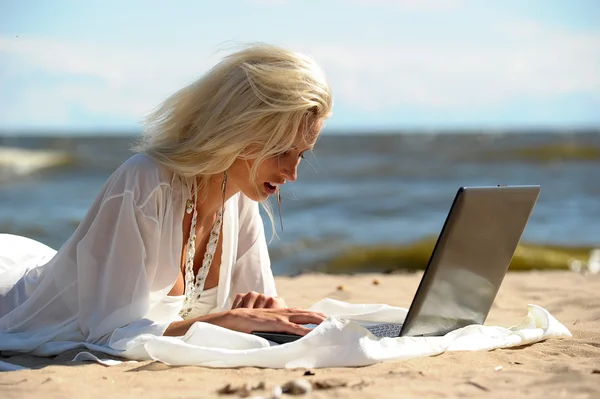 Bir dizüstü bilgisayar ile bir plajda mutlu sarışın kadın — Stok fotoğraf